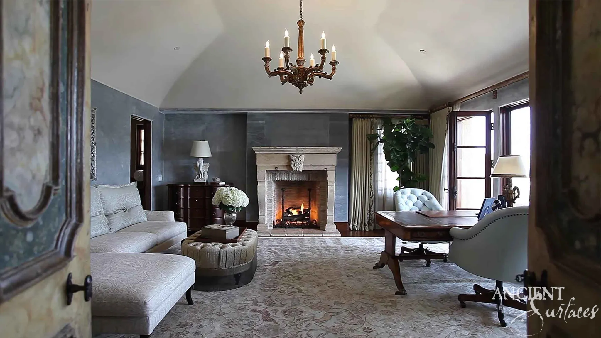Grand reclaimed antique limestone fireplace mantel with a lit hearth in an elegant room