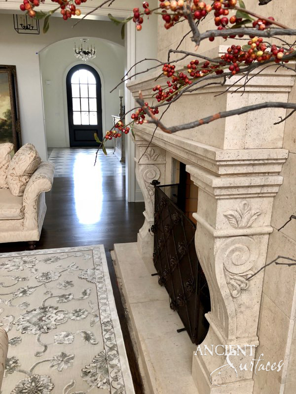 Reclaimed antique limestone fireplace mantel with carved foliate scroll jambs in a light-filled entry hall