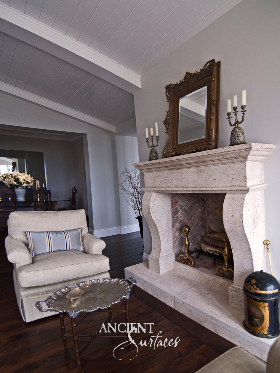 Cream limestone fireplace mantel on carved scroll corbels styled with a gilt mirror and candelabra